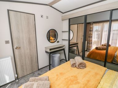 A bedroom with a bed covered in orange blanket and folded towels a dressing table with round mirror and sliding mirrored wardrobe at Puffin Lodge in Broad Haven