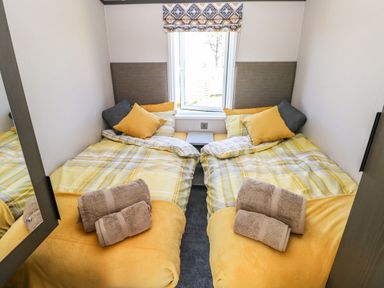 A bedroom with two single beds yellow bedding and towels on the beds at Puffin Lodge in Broad Haven