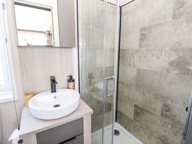 A bathroom with a sink and faucet next to a glass shower enclosure with tiled walls at Puffin Lodge in Broad Haven