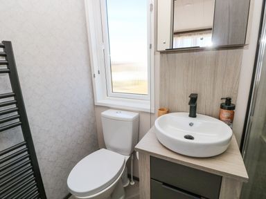 A bathroom with a toilet a sink with a faucet a mirror and a window at Puffin Lodge in Broad Haven
