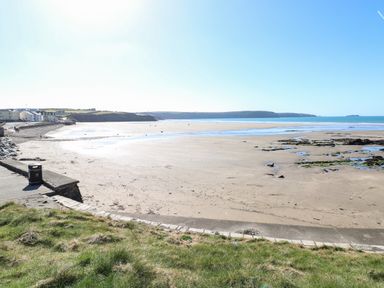 A sandy beach with rocks and water near houses and grassy area at Puffin Lodge in Broad Haven