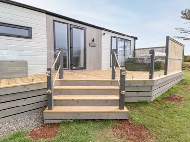 A wooden deck with stairs and rope railings outside a building with glass doors and windows at Puffin Lodge in Broad Haven