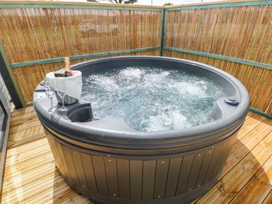 A round outdoor hot tub with bubbling water a bottle of champagne in an ice bucket and two glasses on a wooden deck at Puffin Lodge in Broad Haven