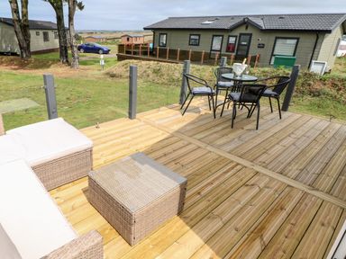 A wooden deck with outdoor seating and a table with chairs beside a house in Broad Haven