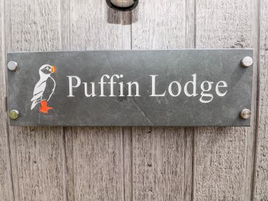 A sign with a puffin illustration and the text Puffin Lodge on a wooden wall at Puffin Lodge in Broad Haven