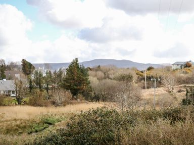 A rural landscape with houses trees and hills under a cloudy sky at Wisteria Cottage in Annagry County Donegal