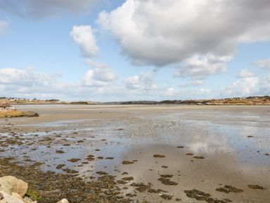 A coastal landscape with a sandy shore and patches of seaweed under a partly cloudy sky at Wisteria Cottage in Annagry County Donegal