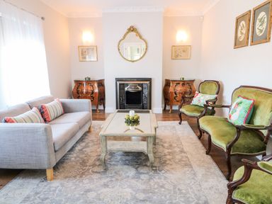 A living room with a gray sofa green upholstered chairs a glass coffee table and two wooden cabinets at Wisteria Cottage in Annagry County Donegal