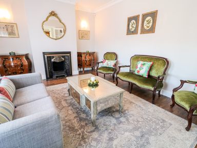A living room with a gray sofa green upholstered chairs a coffee table fireplace and a patterned rug at Wisteria Cottage in Annagry County Donegal