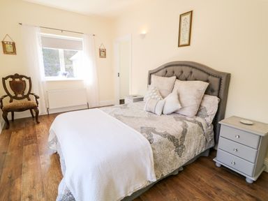 A bedroom with a bed pillows a chair window and bedside tables at Wisteria Cottage in Annagry County Donegal