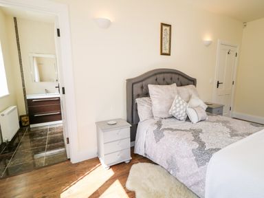 A bedroom with a gray bed and pillows beside bedside tables and an open door leading to a bathroom at Wisteria Cottage in Annagry County Donegal