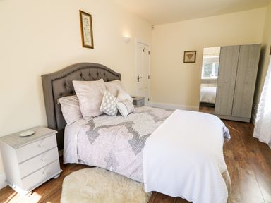 A bedroom with a bed with multiple pillows a bedside table a wardrobe with a mirror and framed pictures on the walls at Wisteria Cottage in Annagry County Donegal