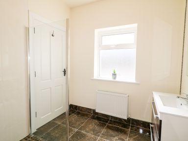 A bathroom with a white door a frosted window a radiator a small plant on the windowsill a white sink and dark tiled floor at Wisteria Cottage in Annagry County Donegal