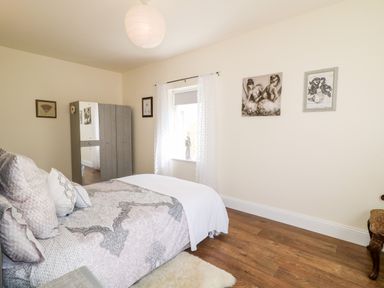 A bedroom with a bed a wardrobe window and framed pictures at Wisteria Cottage in Annagry County Donegal
