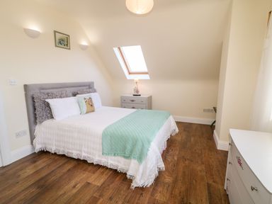 A bedroom with a double bed a nightstand with a lamp a skylight window and wooden flooring at Wisteria Cottage in Annagry County Donegal