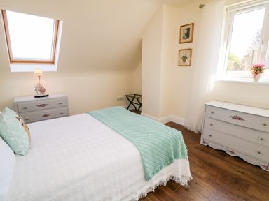 A bedroom with a bed and two dressers under a skylight and window at Wisteria Cottage in Annagry County Donegal