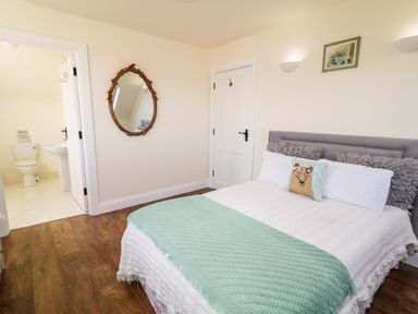A bedroom with a bed with pillows a green throw a mirror on the wall and an open door to a bathroom at Wisteria Cottage in Annagry County Donegal