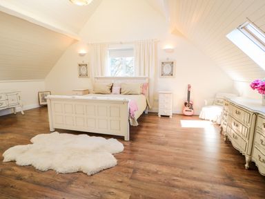 A bedroom with a bed a white rug wooden floor a pink guitar and dressers at Wisteria Cottage in Annagry County Donegal