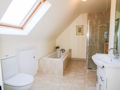 A bathroom with a toilet bathtub shower and sink under a skylight at Wisteria Cottage in Annagry County Donegal