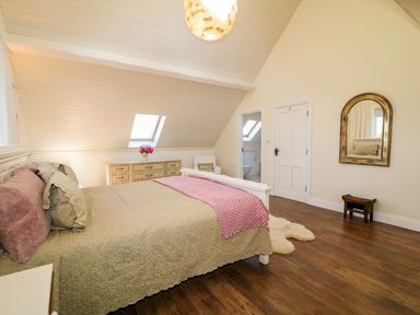 A bedroom with a bed beige and pink bedding a dresser a chair a mirror and wooden floor at Wisteria Cottage in Annagry County Donegal