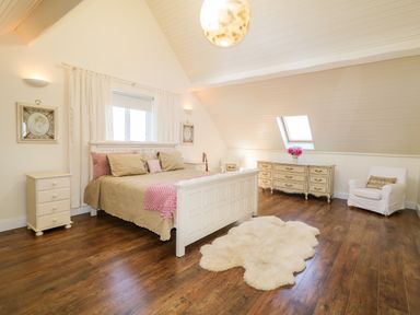 A bedroom with a bed a nightstand a dresser an armchair and a rug on wooden floor at Wisteria Cottage in Annagry County Donegal
