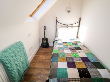 A small bedroom with a single bed covered by a colorful patchwork quilt a guitar in the corner and a green knitted blanket on a radiator at Wisteria Cottage in Annagry County Donegal