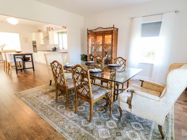 A dining room with a glass table and wooden chairs next to a decorated cabinet at Wisteria Cottage in Annagry County Donegal