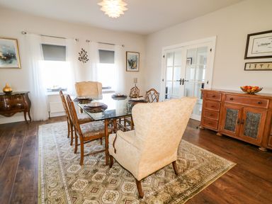 A dining room with a glass table and upholstered chairs on a patterned rug at Wisteria Cottage in Annagry County Donegal