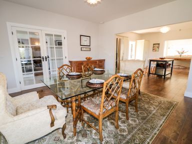 A dining room with a glass table surrounded by wooden chairs and armchairs at Wisteria Cottage in Annagry County Donegal