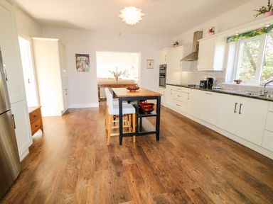 A kitchen with wooden floor white cabinets a kitchen island with stools and a window at Wisteria Cottage in Annagry County Donegal