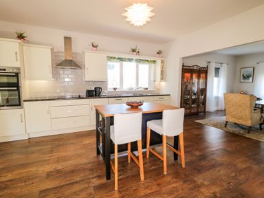 A kitchen with an island and two chairs next to a dining area with an armchair and a glass cabinet at Wisteria Cottage in Annagry County Donegal