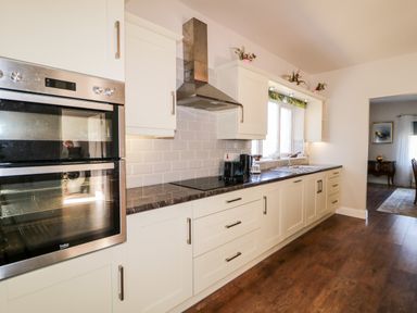 A kitchen with white cabinets a double oven a stove and a sink at Wisteria Cottage Annagry County Donegal