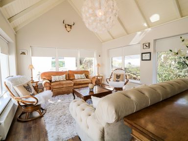 A living room with sofas chairs a wooden coffee table and large windows at Wisteria Cottage in Annagry County Donegal