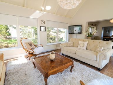 A living room with a beige sofa a wooden coffee table and large windows at Wisteria Cottage in Annagry County Donegal