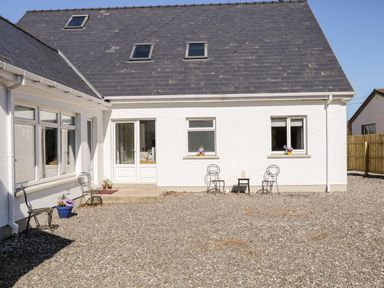 Front view of a white house with a gravel courtyard metal chairs small tables and flower pots at Wisteria Cottage in Annagry County Donegal