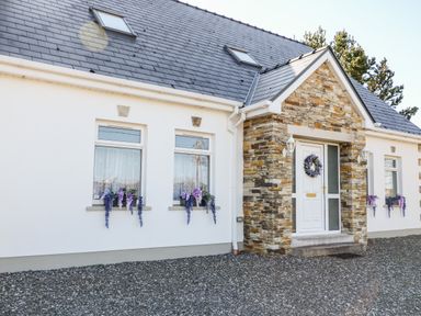 A white house with stone entrance and windows with flower pots at Wisteria Cottage in Annagry County Donegal