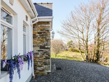 Exterior side of a house with flower boxes on windows and trees in the background at Wisteria Cottage in Annagry County Donegal