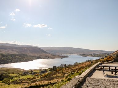 A river flowing through a valley with hills and houses on the side and a bench overlooking the river at Wisteria Cottage in Annagry County Donegal