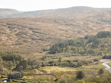A stone church near a river surrounded by trees and hills at Wisteria Cottage in Annagry County Donegal