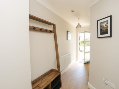 A hallway with a wooden coat rack bench light fixture open door and framed pictures at 4 Pen Llanw Tides Reach in Rhosneigr