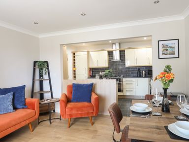 A living room with orange armchairs and blue cushions next to a wooden dining table set with dishes and glasses at 4 Pen Llanw Tides Reach in Rhosneigr