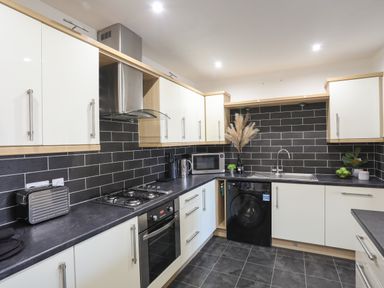 A kitchen with black tiled backsplash white cabinets and stainless steel appliances at 4 Pen Llanw Tides Reach in Rhosneigr