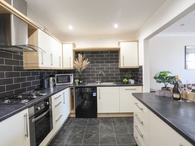A kitchen with black tiled backsplash white cabinets and black countertop at 4 Pen Llanw Tides Reach in Rhosneigr