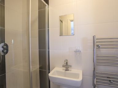 A small bathroom with a shower enclosure sink mirror towel radiator and tile walls at 4 Pen Llanw Tides Reach in Rhosneigr