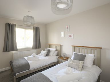 A bedroom with two single beds bedside table lamp and window with curtains at 4 Pen Llanw Tides Reach in Rhosneigr