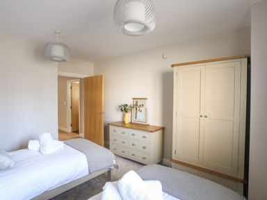 A bedroom with two single beds a dresser a wardrobe and an open wooden door at 4 Pen Llanw Tides Reach in Rhosneigr