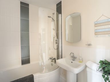 A bathroom with a bathtub shower combination a sink a mirror and a plant at 4 Pen Llanw Tides Reach in Rhosneigr