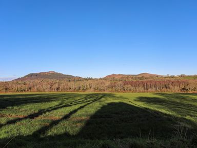A grassy field with shadows of trees and hills in the background at Bryn Moelyn Cottage Yr Efail near Morfa Nefyn