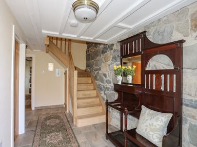 A hallway with wooden stairs a vintage wooden hall stand with a cushion and vases with flowers on a stone wall at Bryn Moelyn Cottage in Yr Efail near Morfa Nefyn