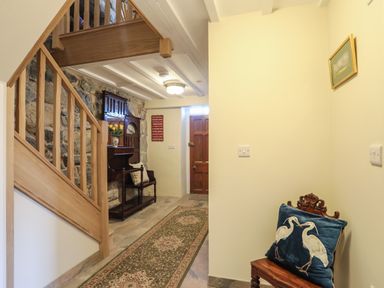 A hallway with wooden staircase a long patterned rug and a wooden bench with a cushion at Bryn Moelyn Cottage in Yr Efail near Morfa Nefyn